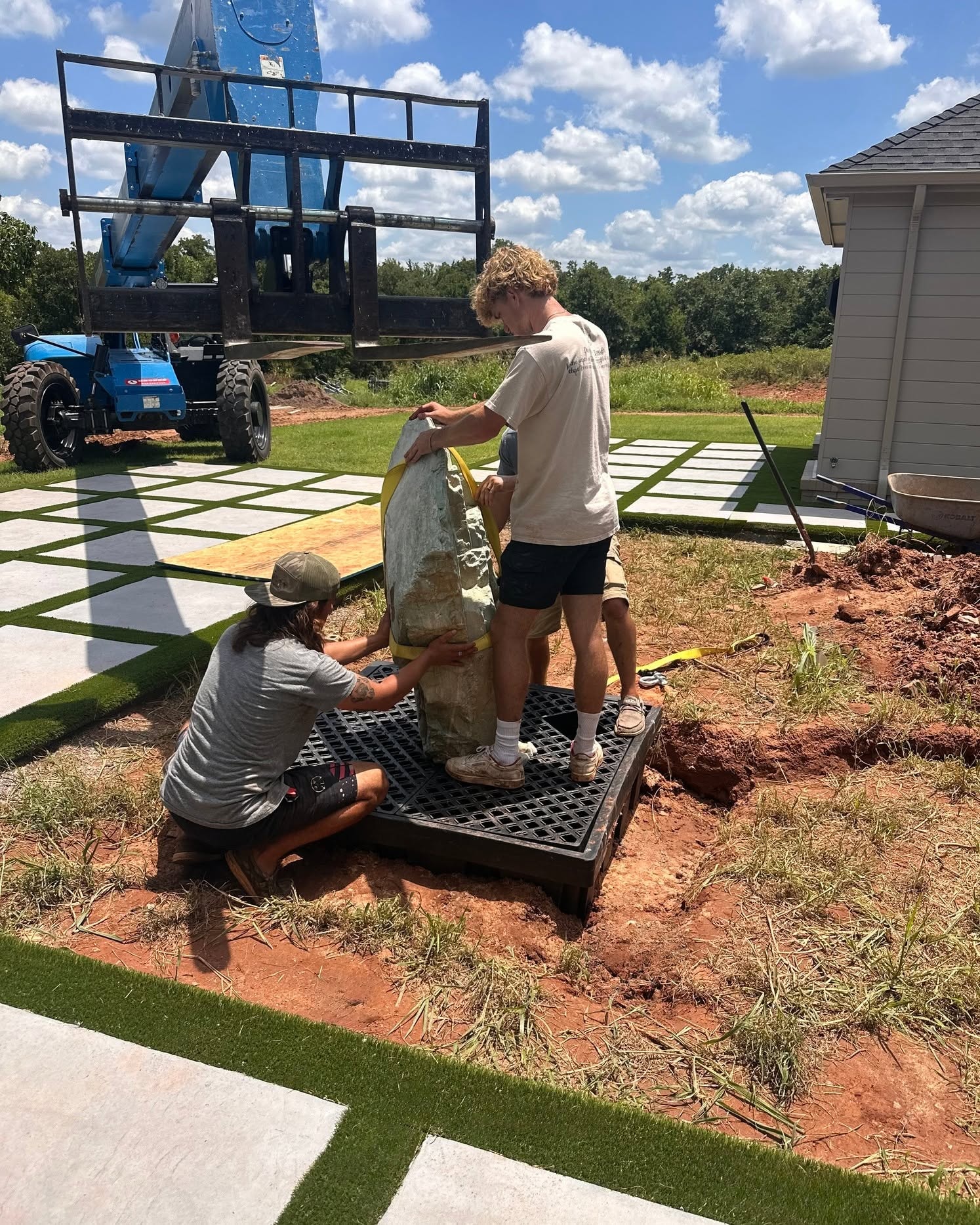 Studio W crew setting a large natural boulder feature on a modern paver and artificial turf installation