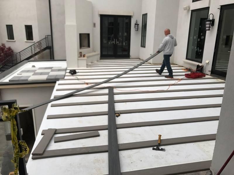 Crew installing composite deck boards in modern white courtyard with checkerboard tile detail