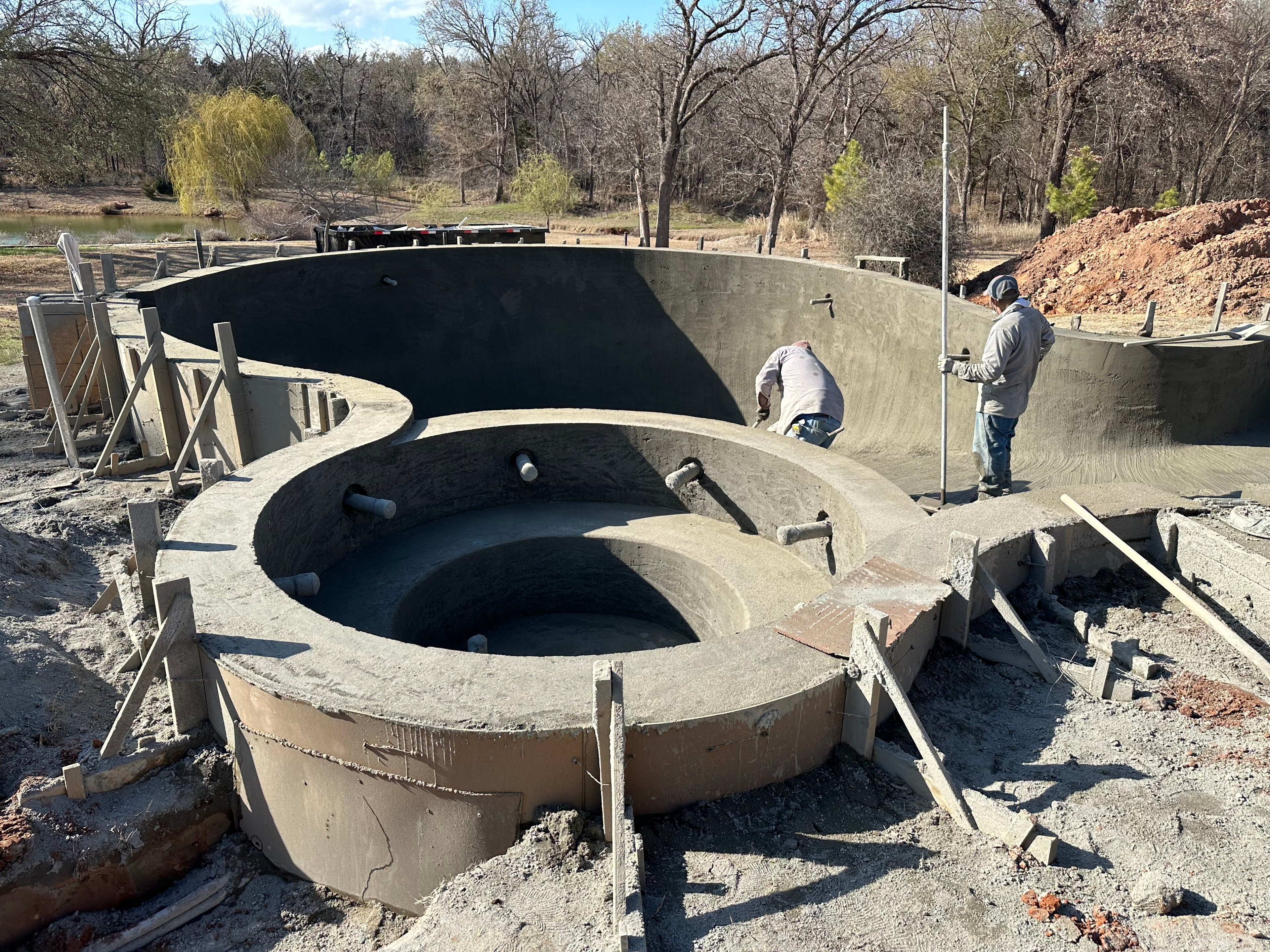 Gunite pool and spa shell under construction on lakeside property with crew finishing concrete