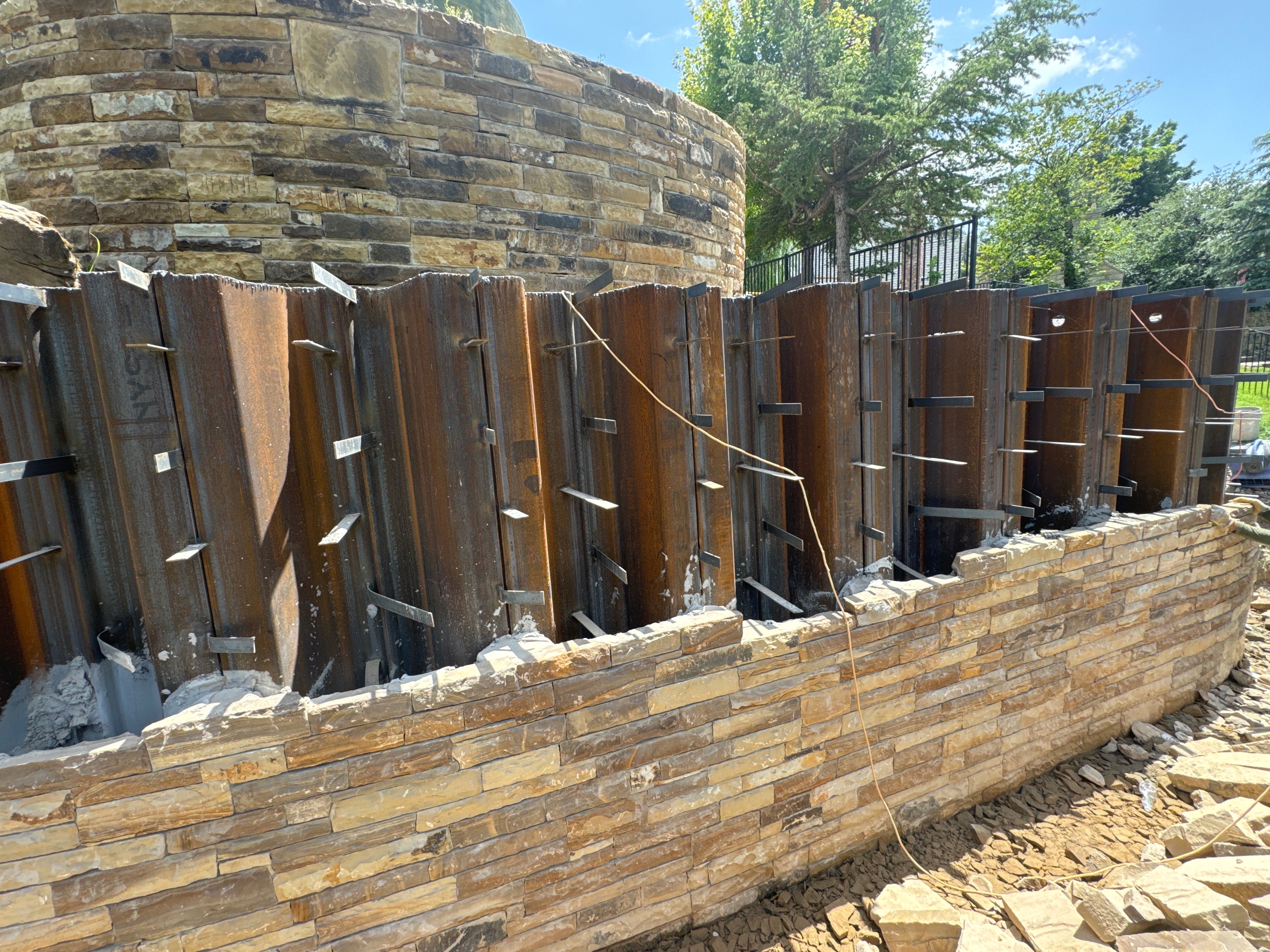 Close-up of curved stone retaining wall with steel sheet pile forms during construction