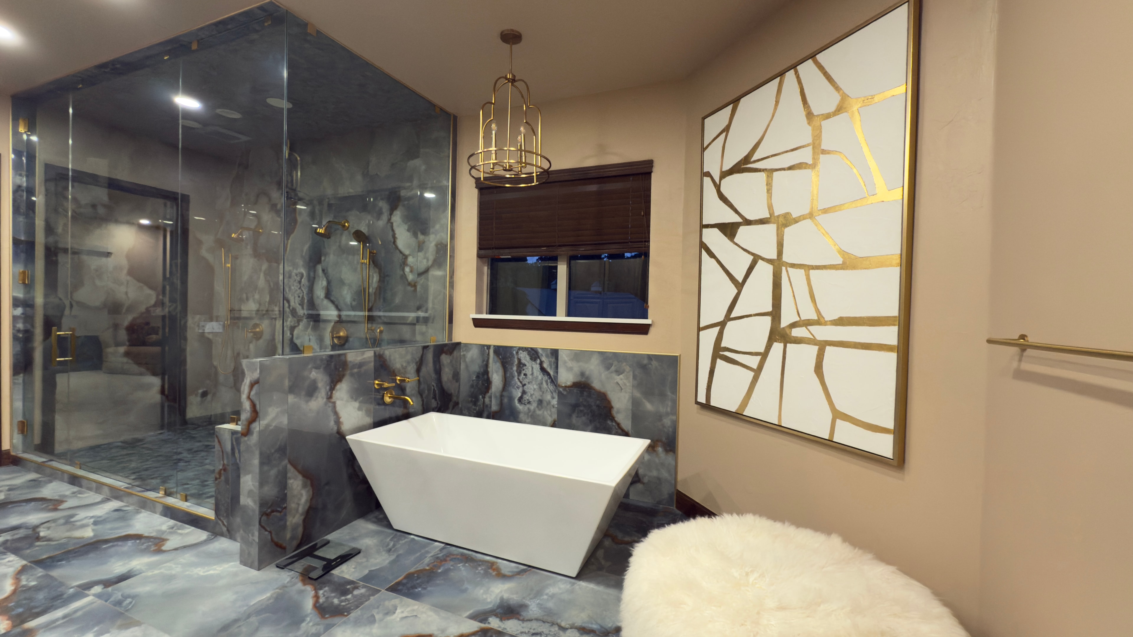 Master bath freestanding soaking tub with marble surround, gold fixtures, and gold-framed art