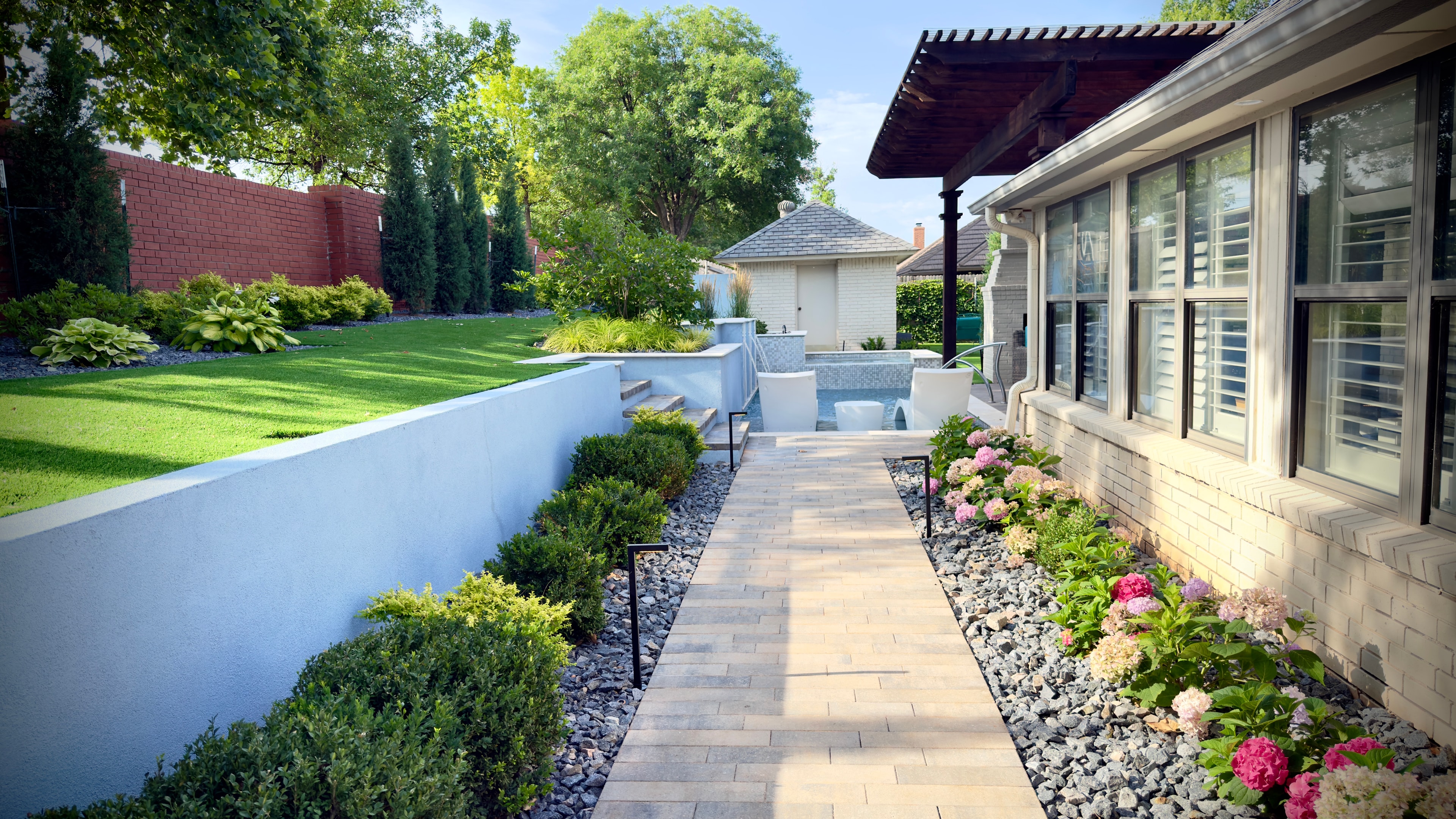 Paver walkway bordered by hydrangeas and boxwoods leading to pool and spa