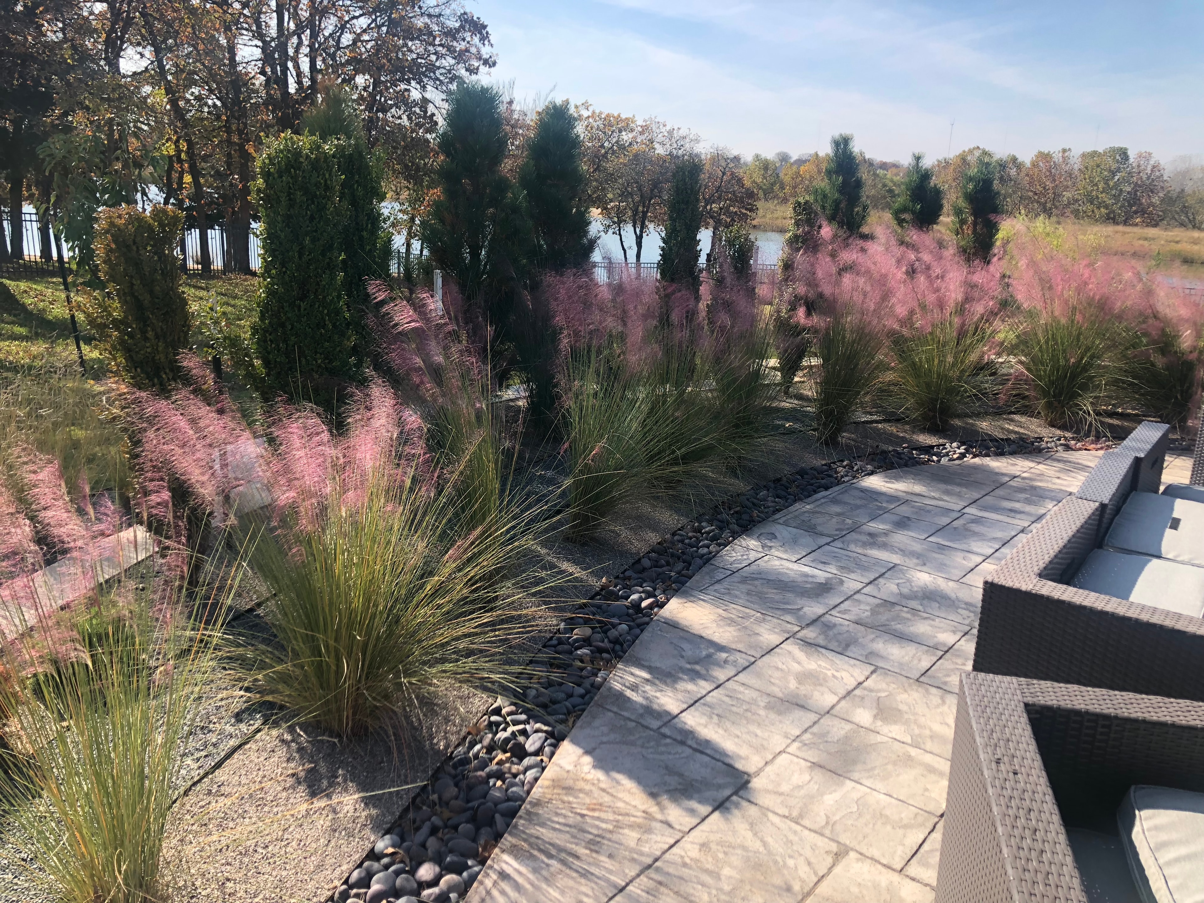 Waterfront patio with pink muhly grass, river rock border, and paver seating area
