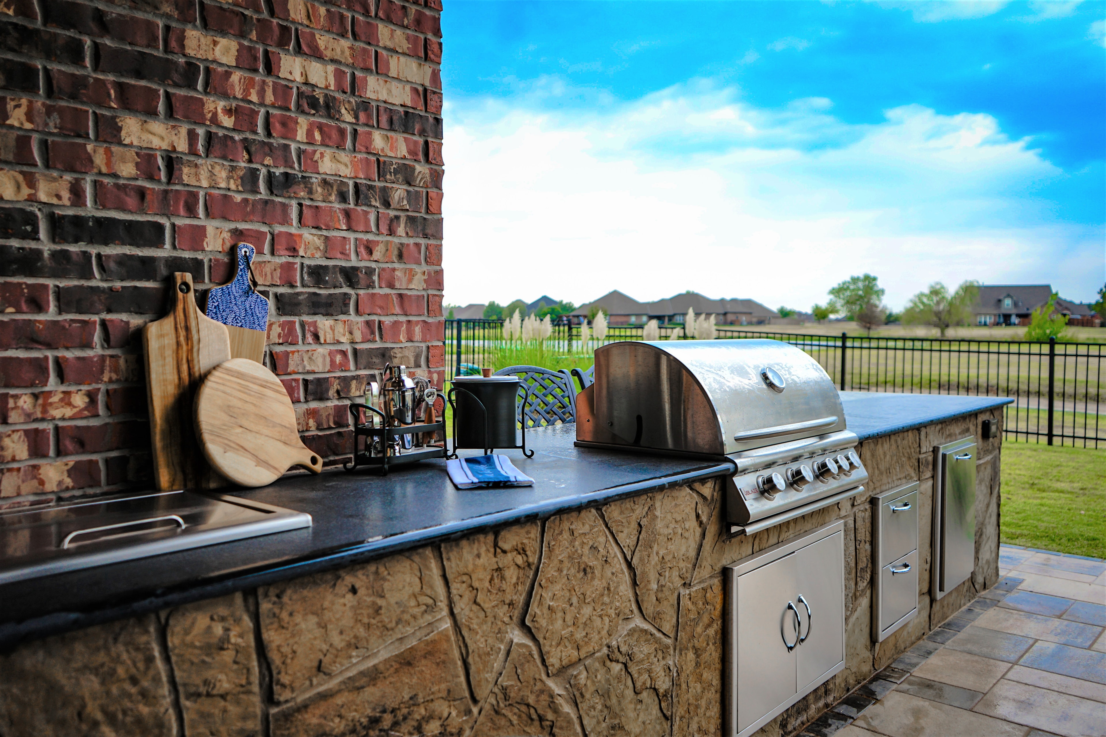 Stone-clad outdoor kitchen with black granite countertop, stainless grill, and brick accent wall