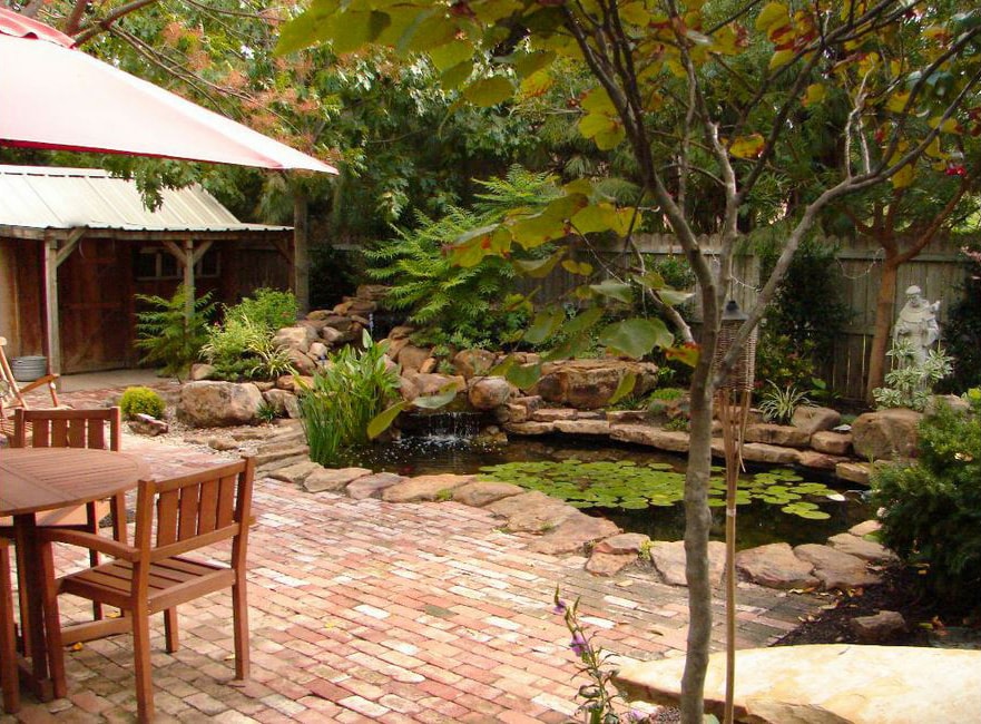 Brick paver patio with lush garden, koi pond, lily pads, and waterfall feature
