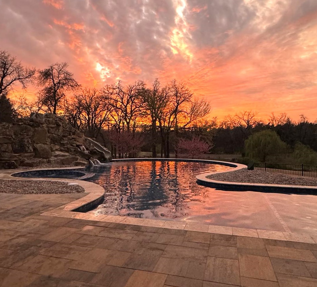 Freeform pool with rock slide and spa reflecting a dramatic fiery sunset sky