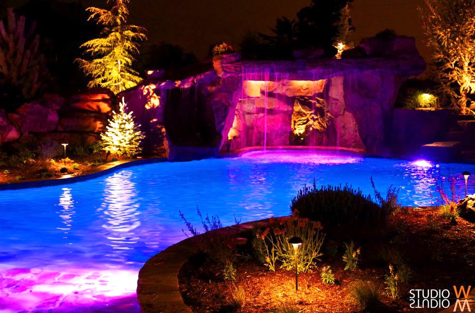 Dramatic grotto pool at night with purple and blue LED lighting and landscape uplighting