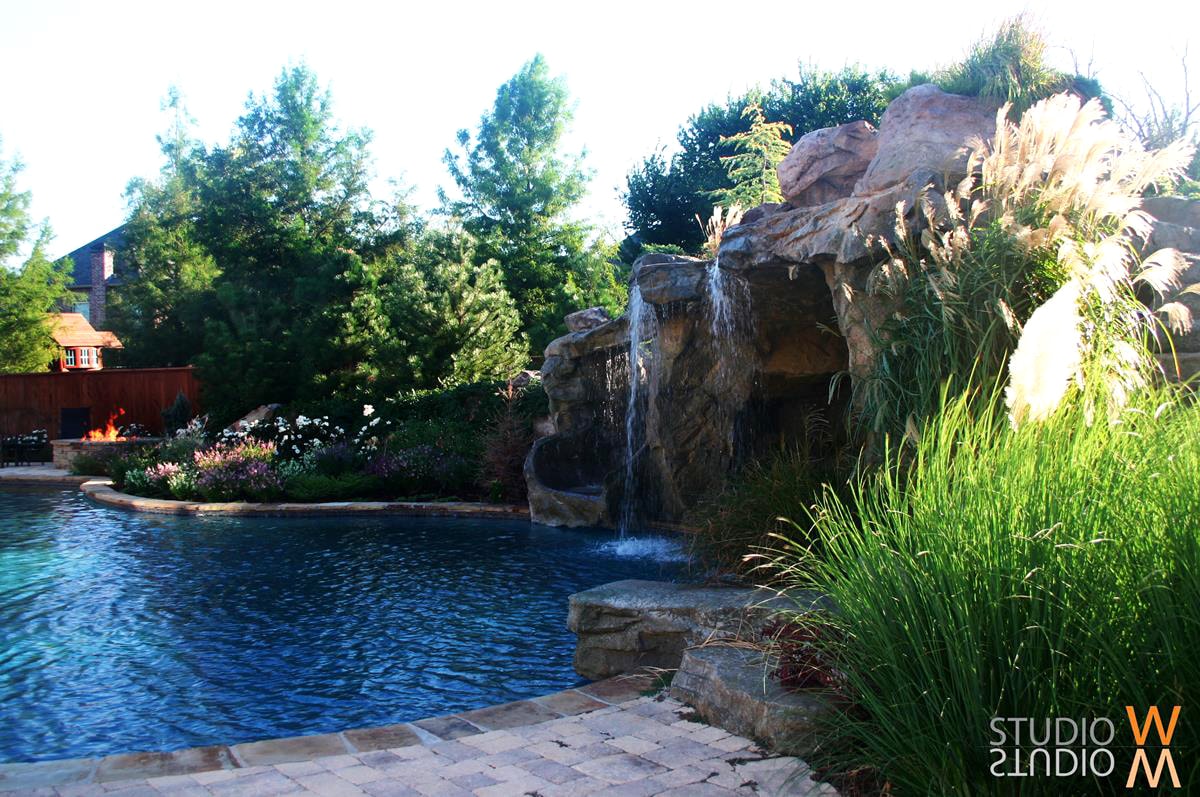 Natural grotto waterfall with lush plantings and fire pit beside a freeform pool