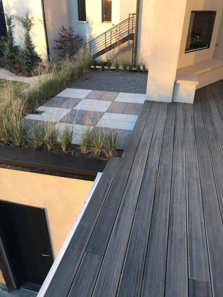 Modern composite deck and large-format paver patio with ornamental grasses and steel railing at dusk