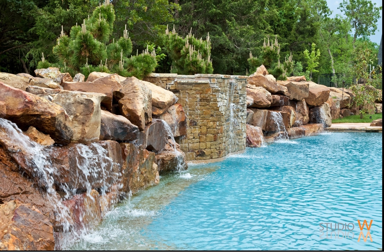 Multi-cascade boulder waterfall with stacked stone pillar feature flowing into bright blue pool