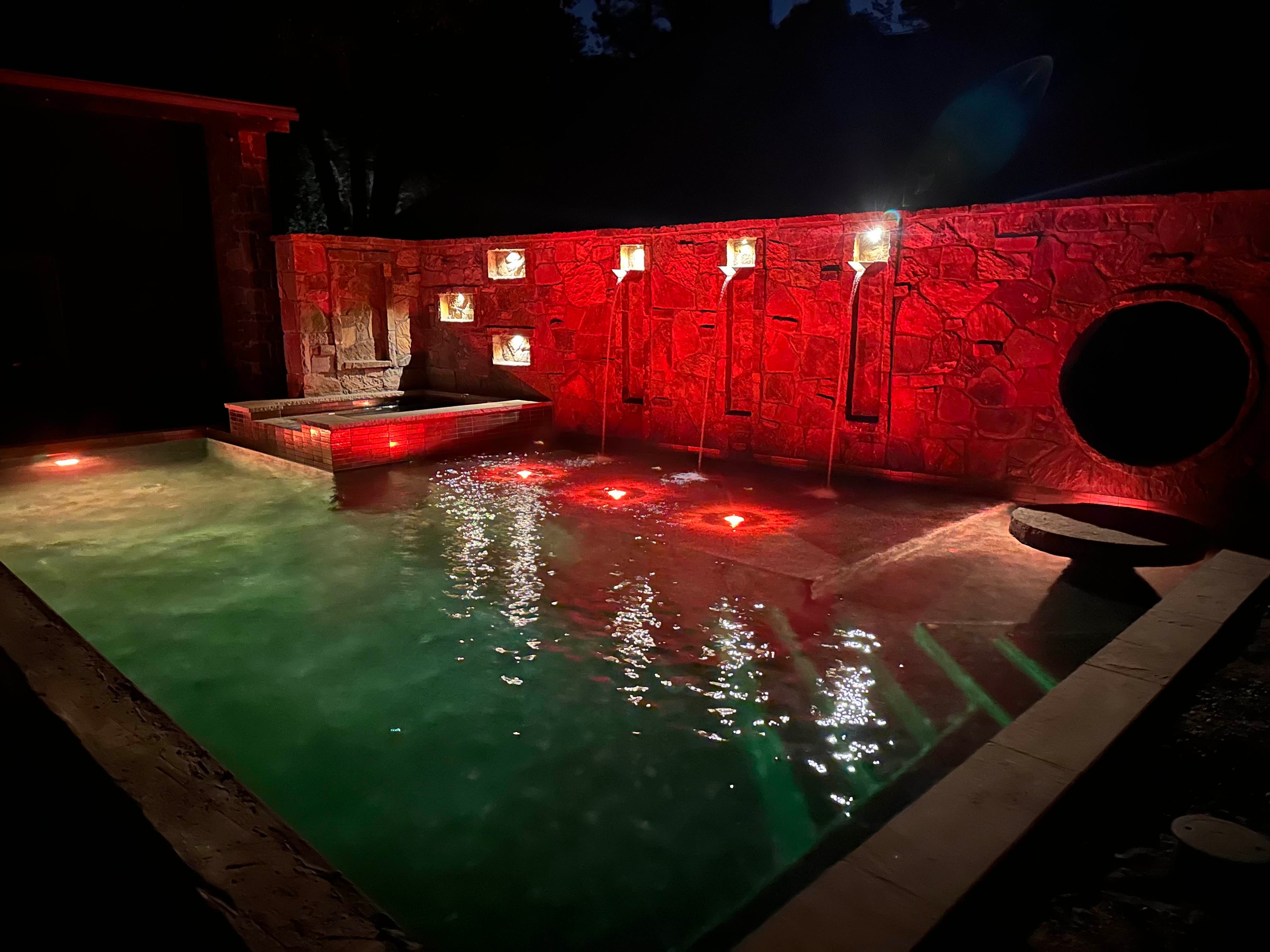 Dramatic nighttime pool with red accent lighting on stone wall and cascading water features