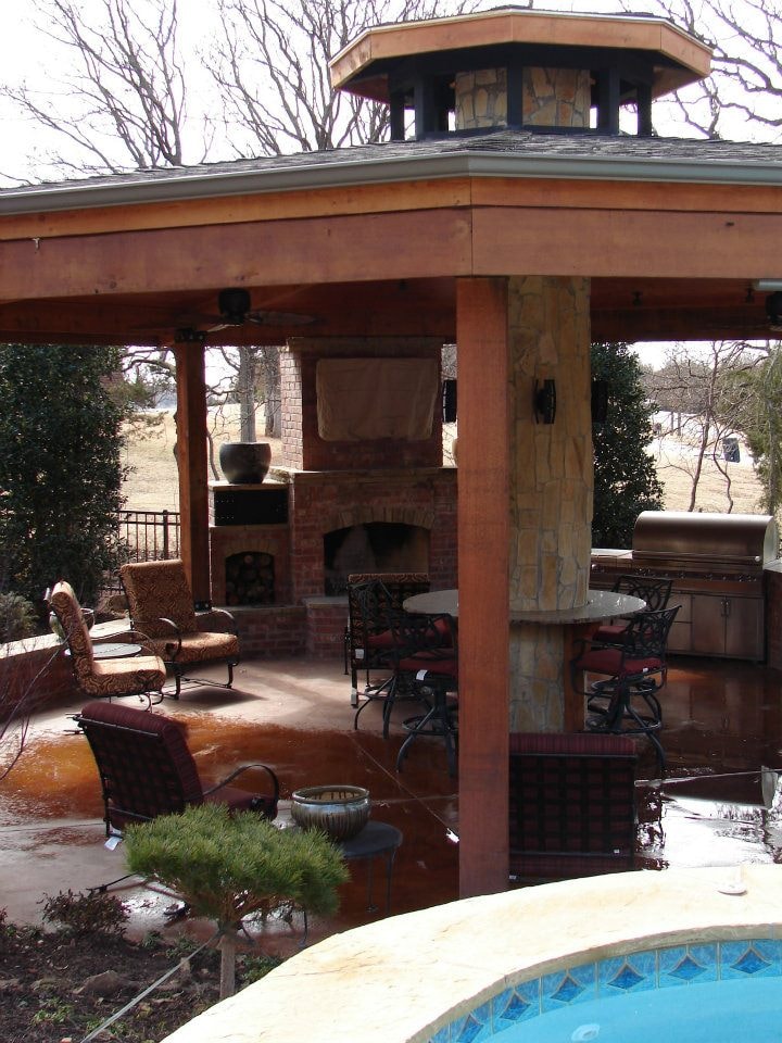 Octagonal cedar pavilion with brick fireplace, ceiling fan, and outdoor kitchen overlooking pool