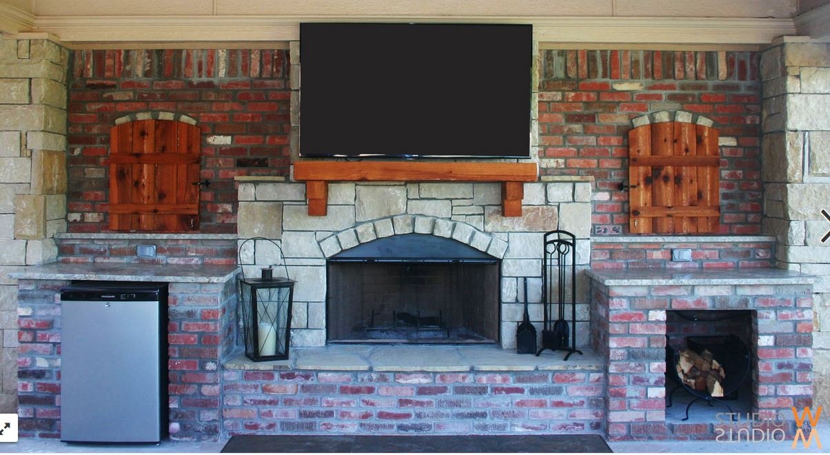 Outdoor fireplace with mounted TV, stone surround, wood mantel, and cedar shutters
