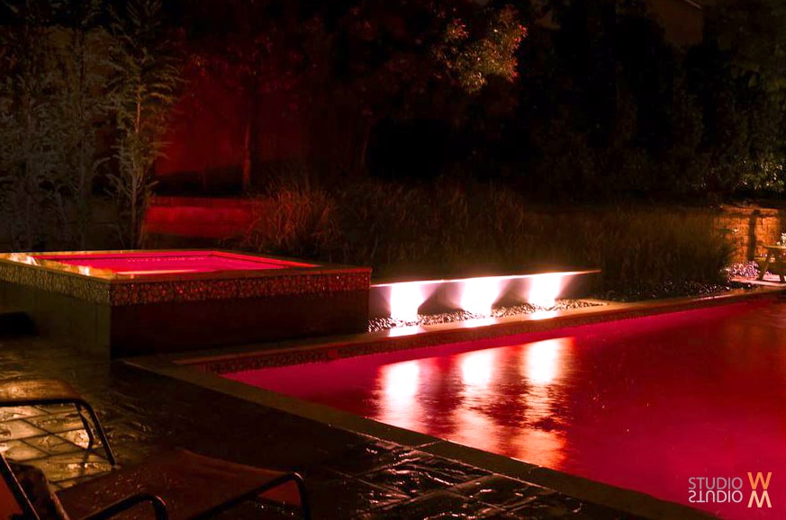 Modern pool and spa with dramatic red LED night lighting and sheet waterfall overflow