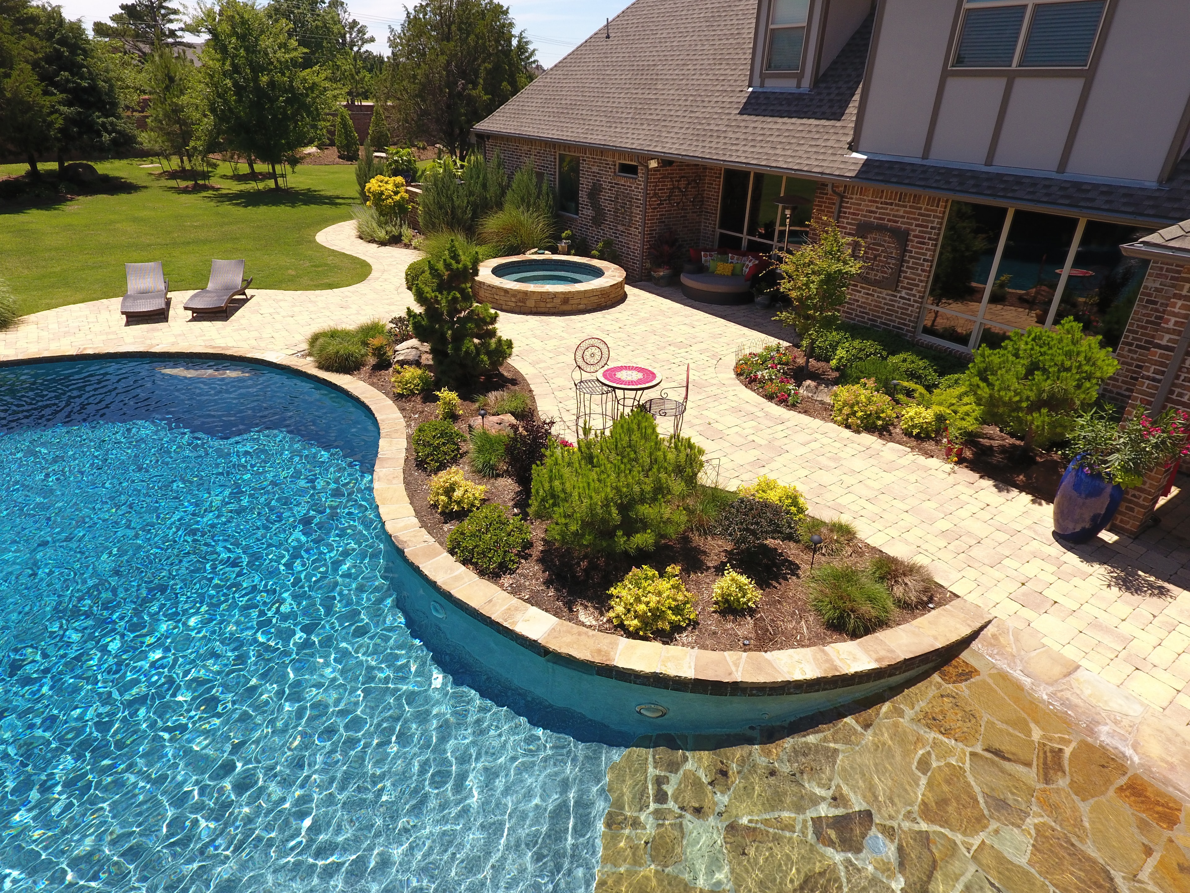Luxury pool and spa with lush landscaping and stone patio