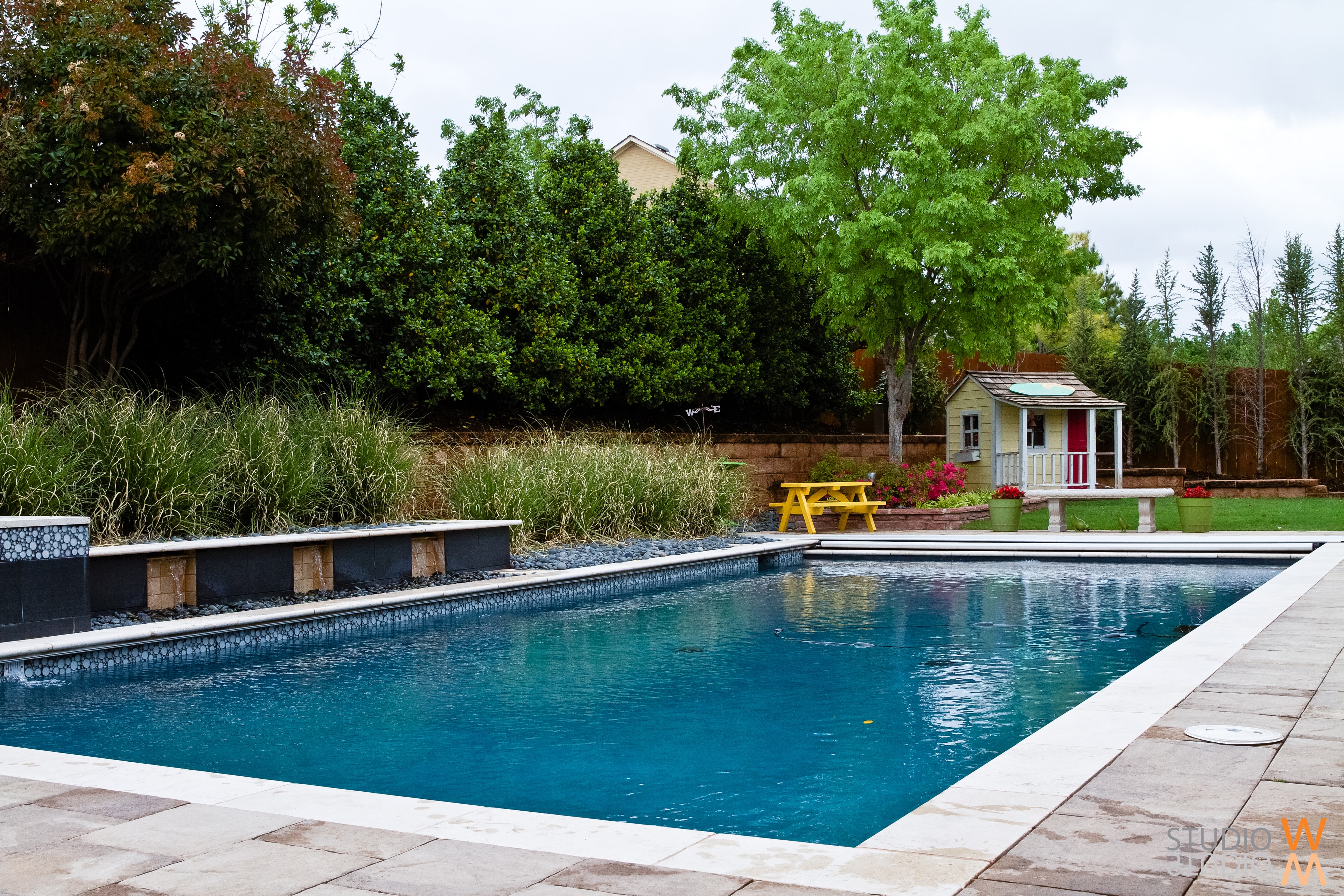 Rectangular pool with ornamental grass retaining wall and charming children's playhouse
