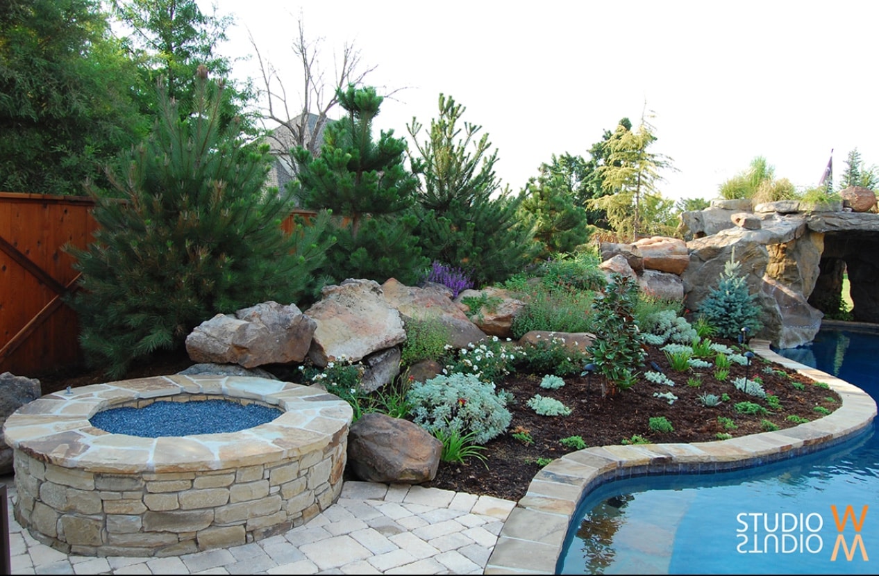 Stone fire pit with xeriscape boulder planting bed and grotto waterfall beyond