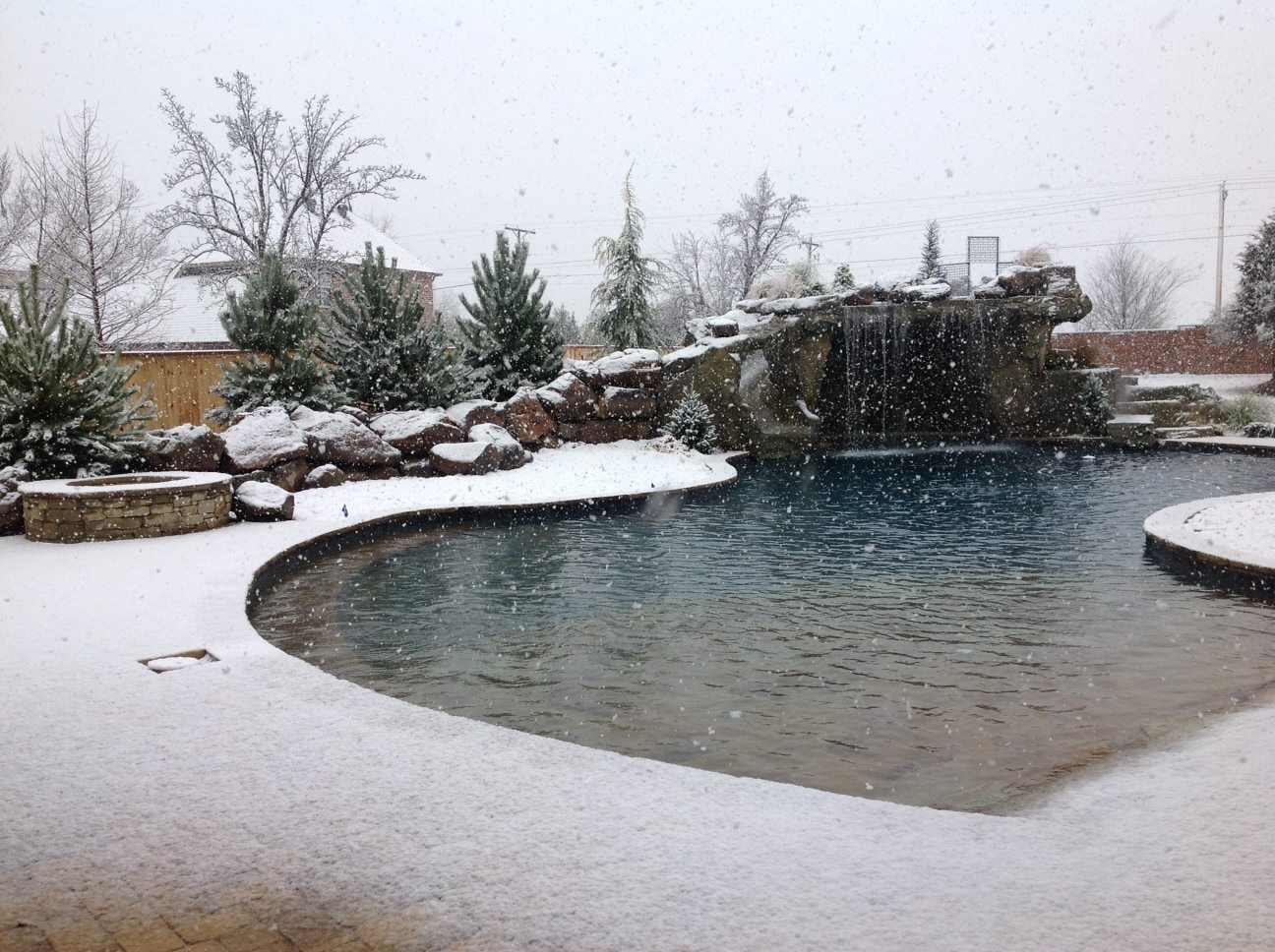 Freeform pool with grotto waterfall and fire pit dusted in fresh snow
